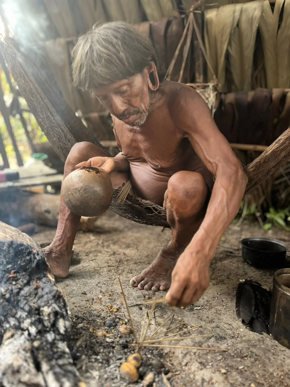 A Waorani host working beside a small fire in a traditional shelter